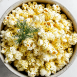 Homemade dill pickle popcorn in a bowl with visible herbs and buttered kernels
