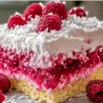 Beautifully plated slice of Raspberry Zinger Poke Cake with whipped topping, raspberry gelatin, and coconut