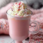 Pink hot chocolate in glass mug with whipped cream and colorful sprinkles