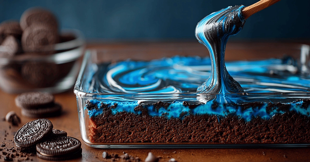 Oreo truffle layer being spread on Blue Velvet Brownies in a glass pan with cookies nearby