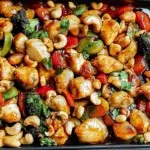 Sheet pan cashew chicken with roasted vegetables and cashews in glossy sauce on baking tray