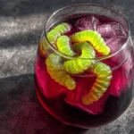 Glass of Witch’s Potion Punch with purple juice, ice cubes, and green gummy worms for Halloween.